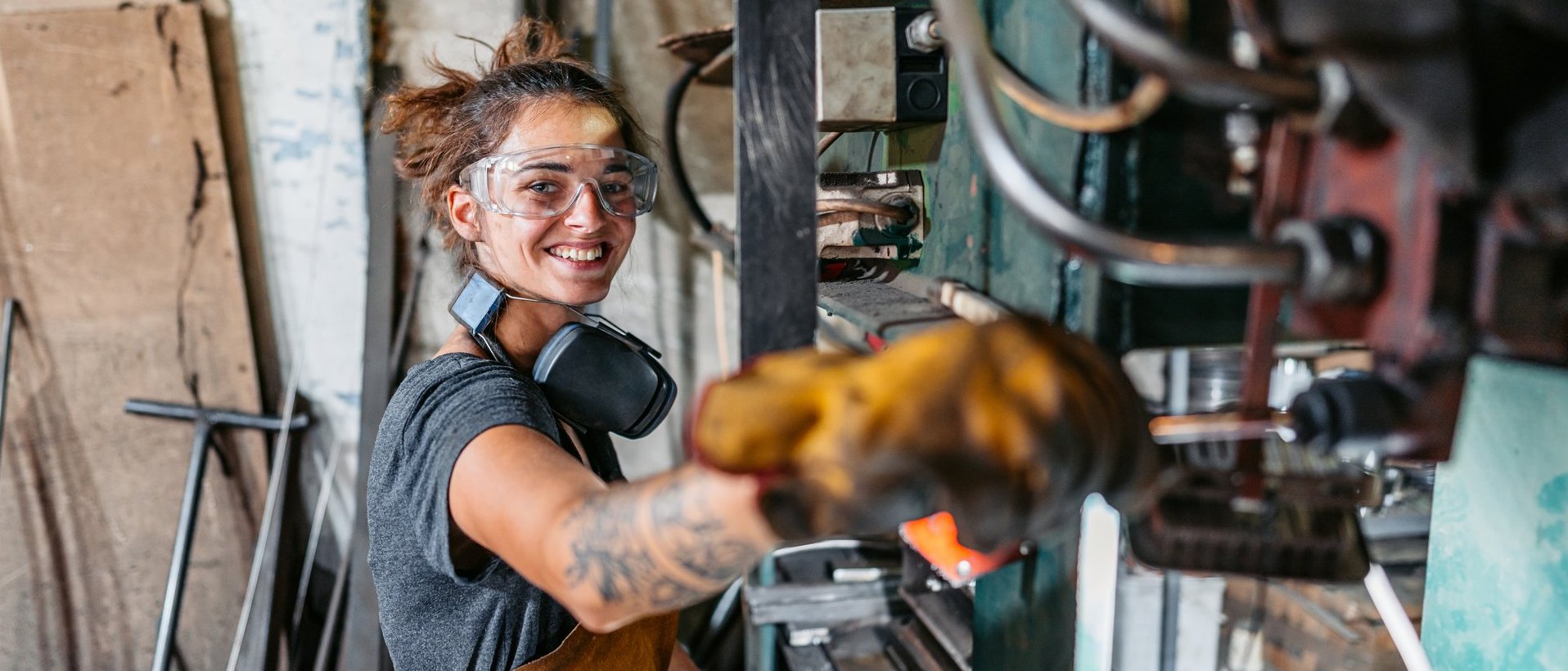 Handwerkerin arbeitet mit Schutzbrille und Gehörschutz an einer Maschine in einer Werkstatt