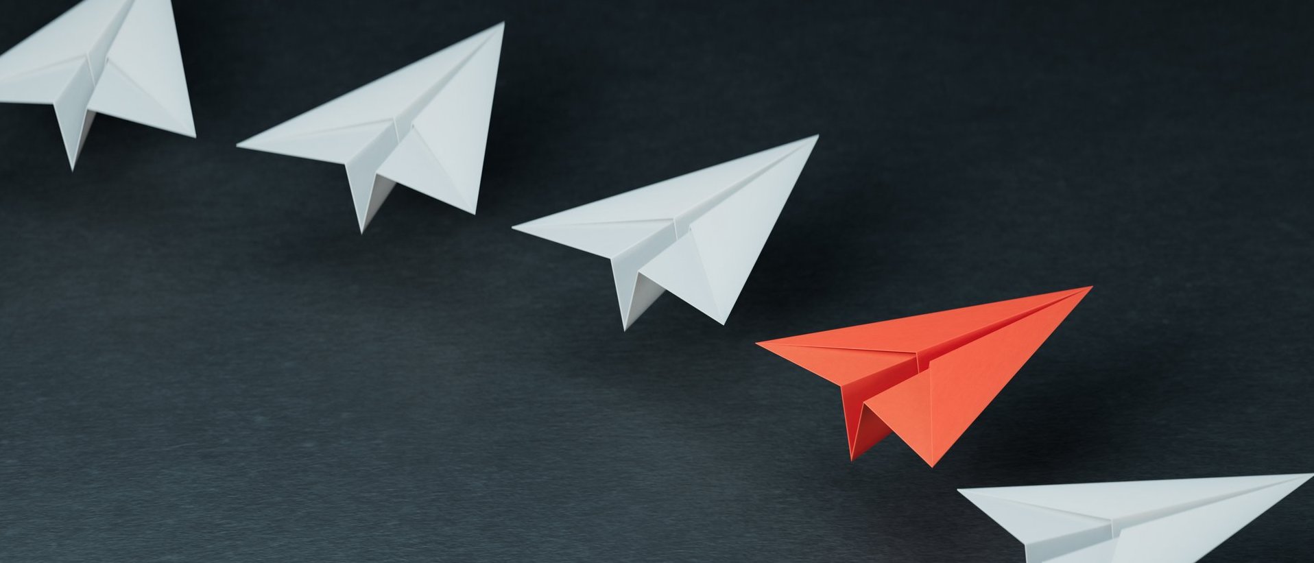 Roter Papierflieger hebt sich zwischen weißen Papierfliegern als Symbol für Führung und neue Wege hervor