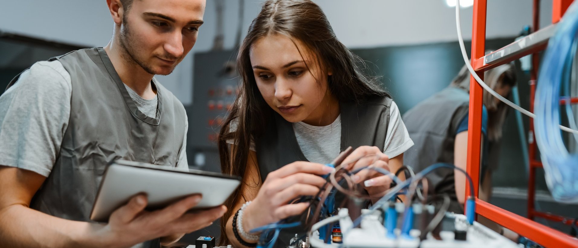 Zwei junge Menschen arbeiten gemeinsam an einer technischen Anlage mit Kabeln und Messgeräten