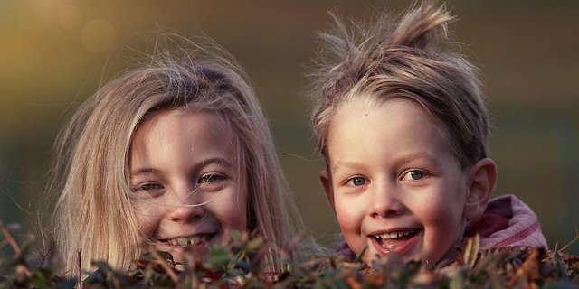 Zwei lachende Kinder schauen hinter Herbstlaub hervor