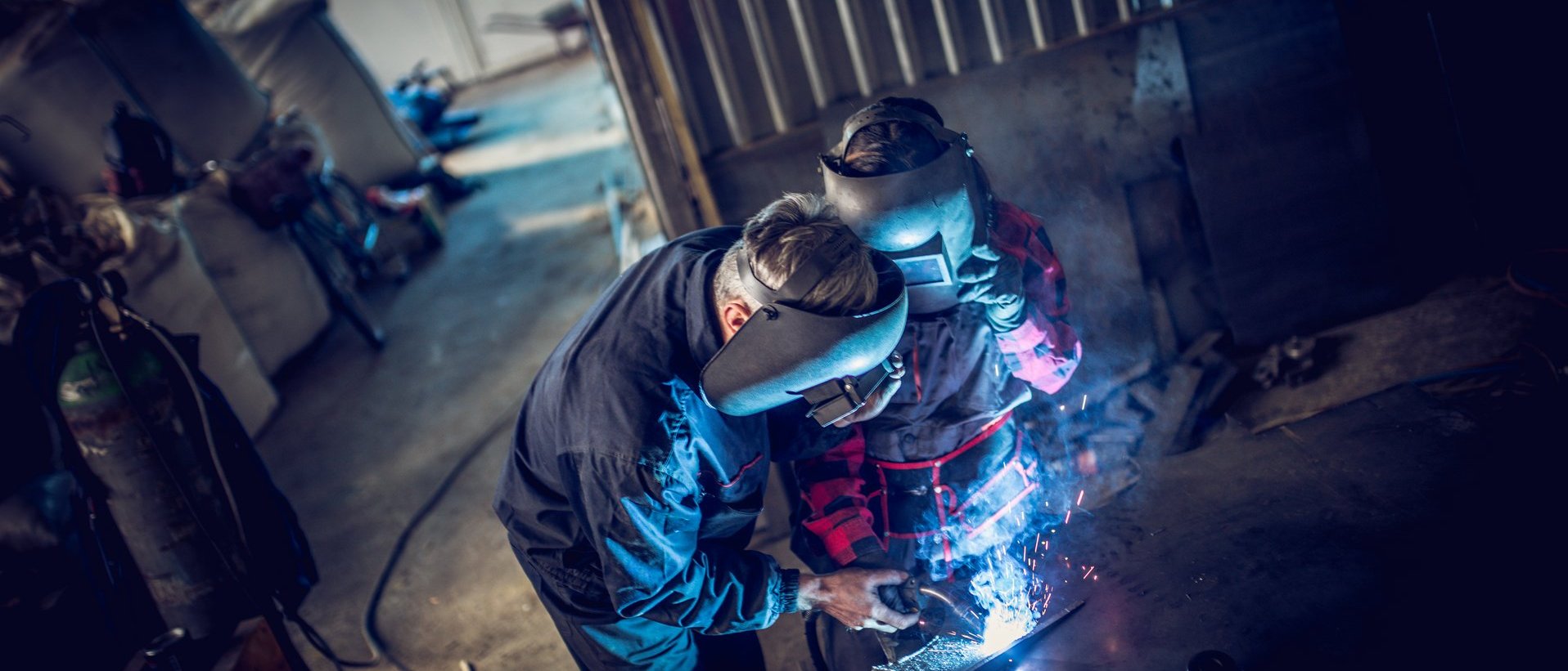 Schweißer arbeitet mit Schutzhelm an einem Metallbauteil in einer Werkstatt