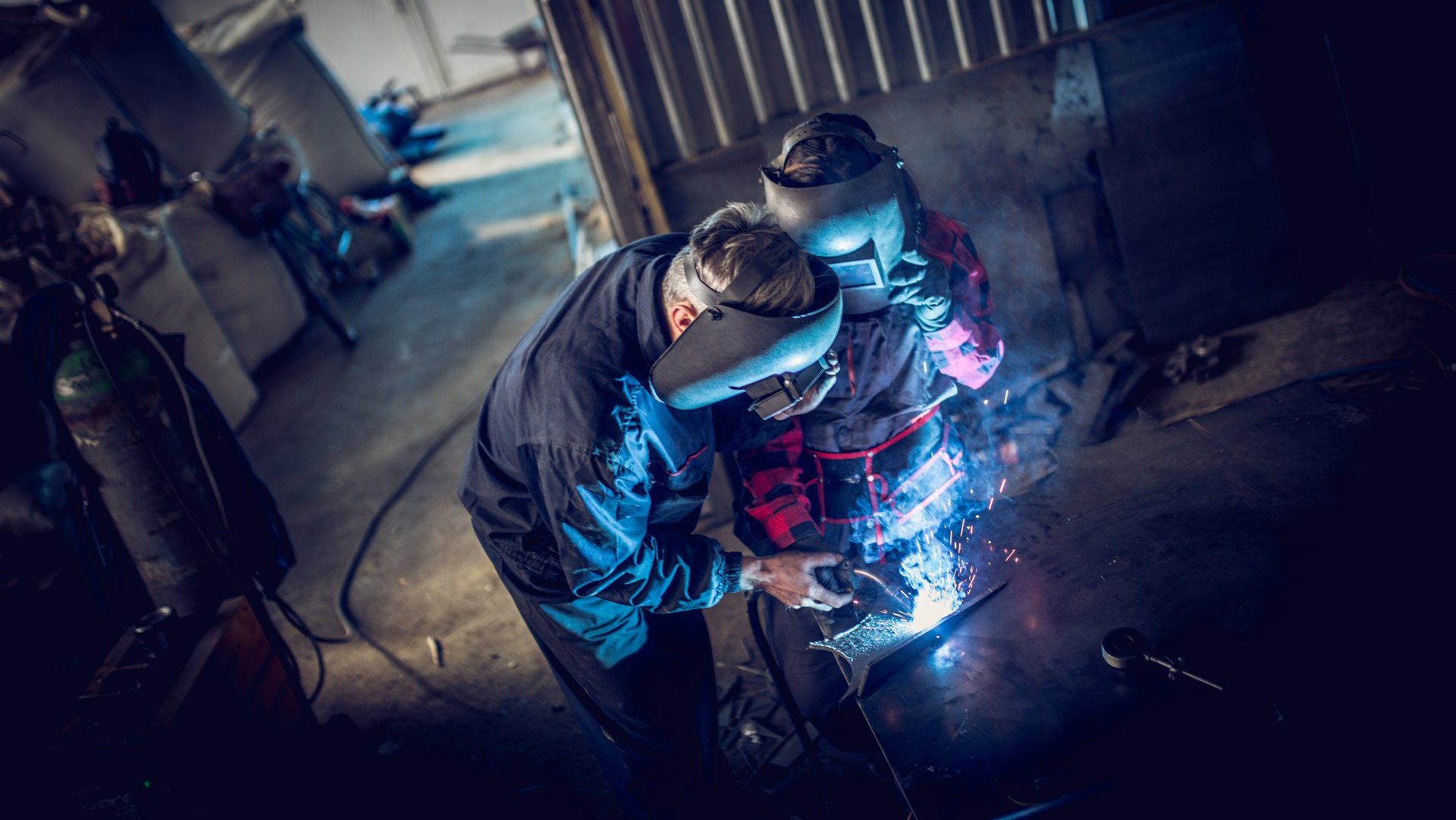 Schweißer arbeitet mit Schutzhelm an einem Metallbauteil in einer Werkstatt