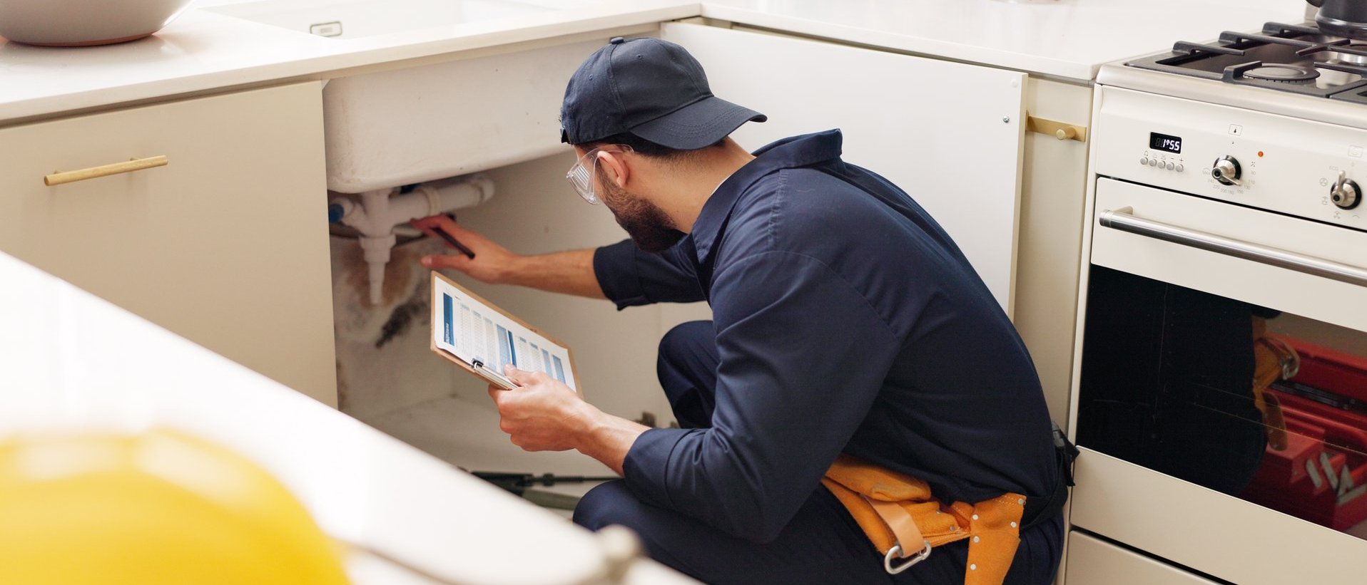 Servicetechniker überprüft mit einem Tablet ein Küchengerät unter der Arbeitsplatte