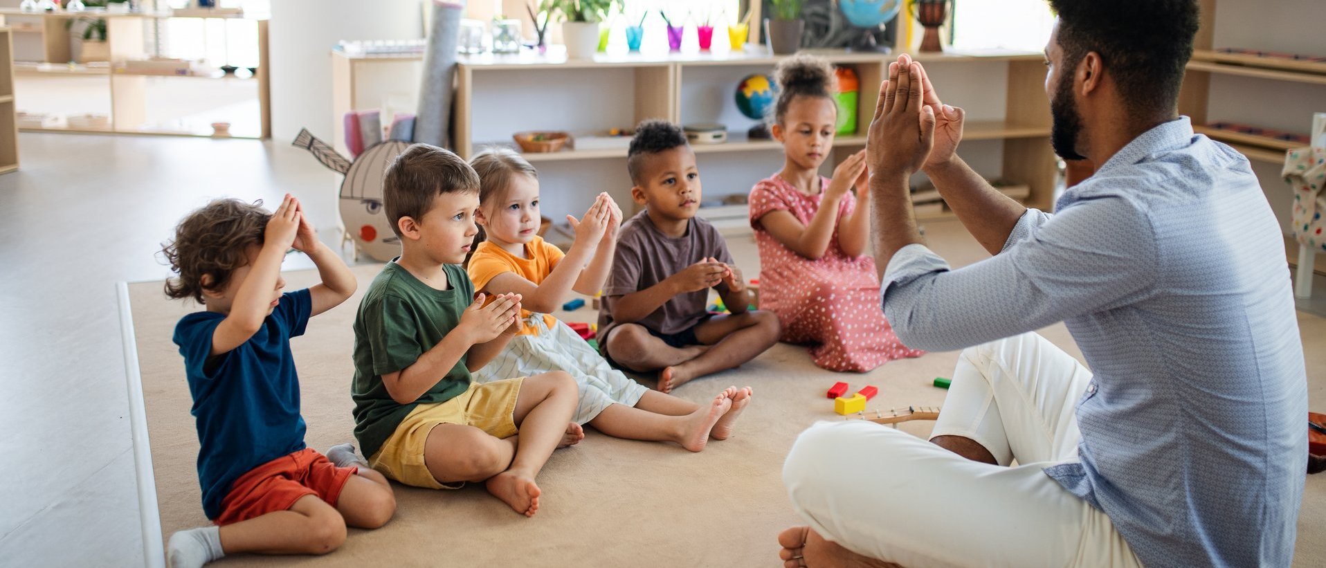 Pädagogische Fachkraft sitzt mit einer Gruppe von Kindern im Kreis und gestaltet eine gemeinsame Aktivität