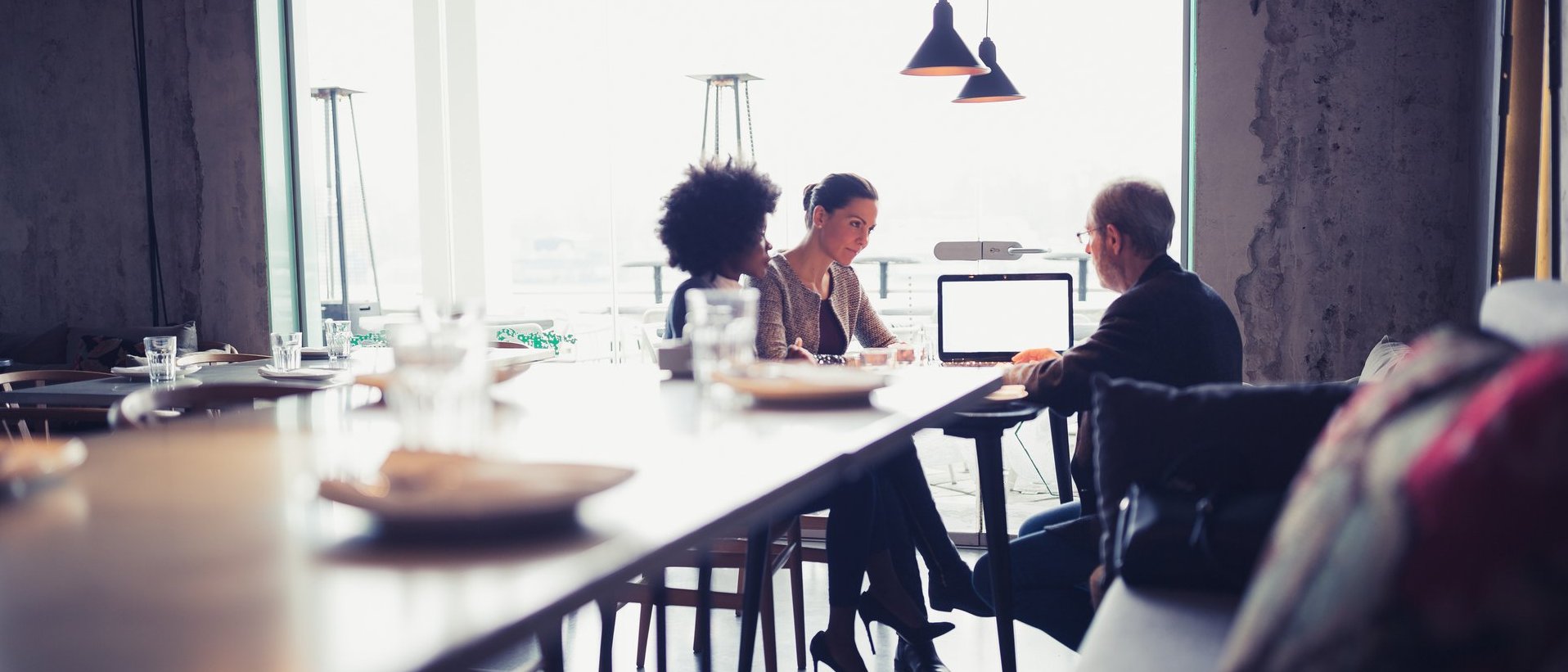 Drei Personen sitzen an einem Tisch und besprechen gemeinsam Inhalte an einem Laptop