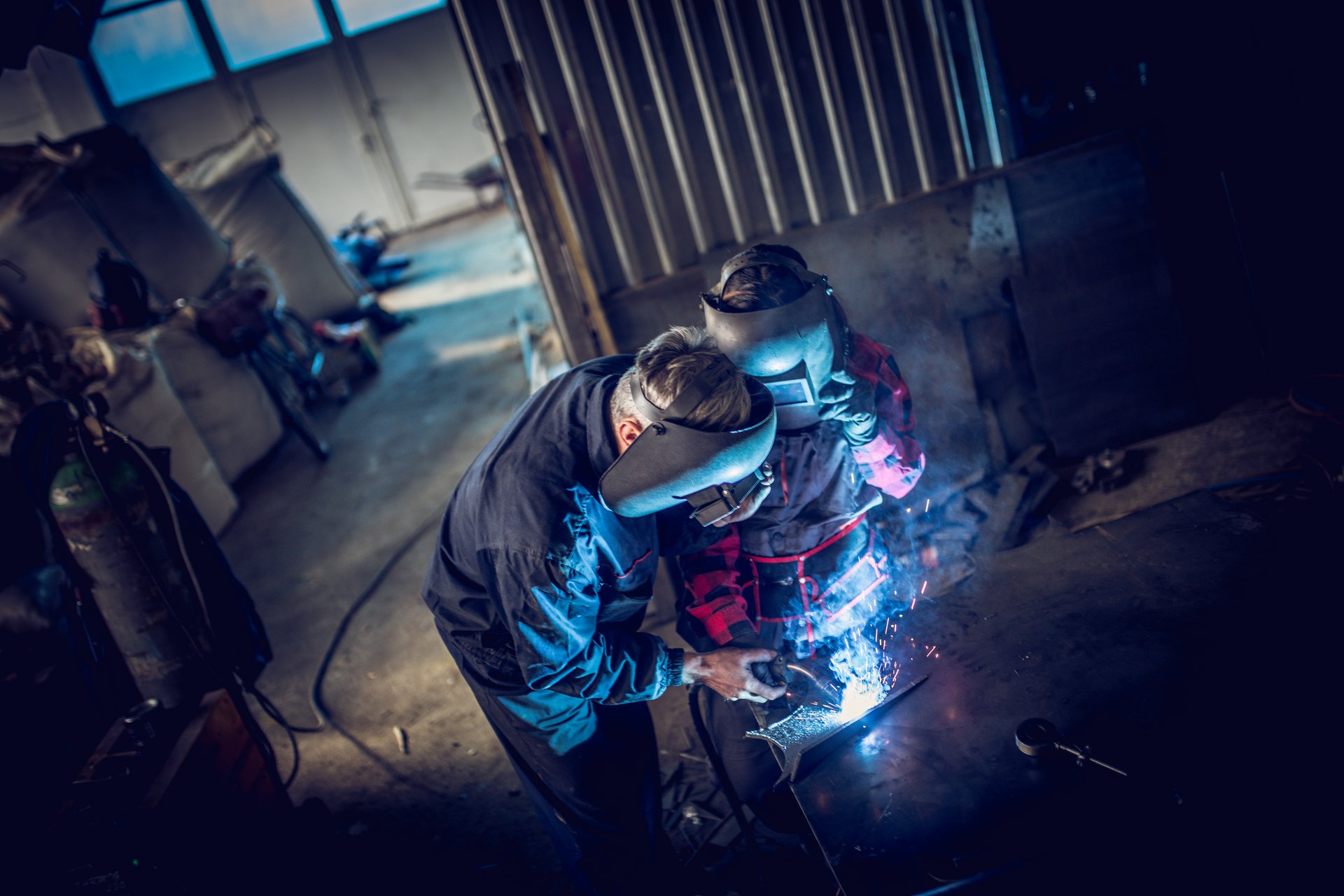 Schweißer arbeitet mit Schutzhelm an einem Metallbauteil in einer Werkstatt