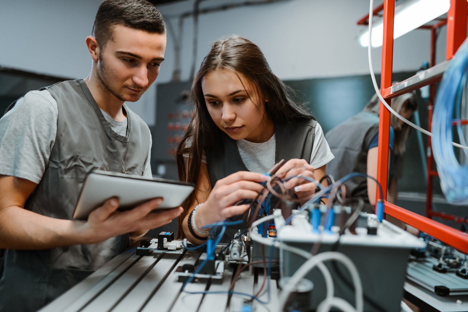 Zwei junge Menschen arbeiten gemeinsam an einer technischen Anlage mit Kabeln und Messgeräten.