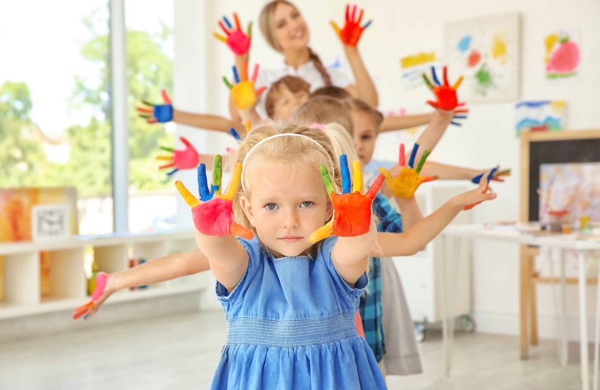 Viele Kinder mit bunt angemalten Händen schauen in die Kamera und strecken die Arme in die Luft