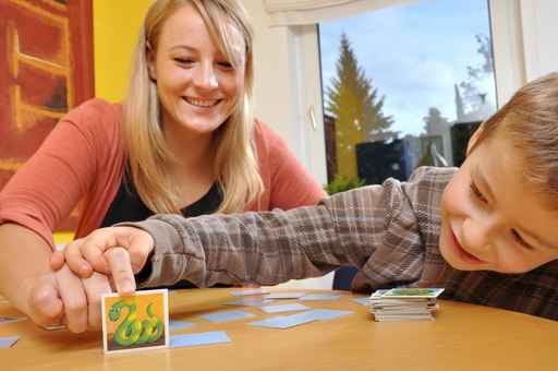 Eine Betreuerin spielt mit einem Jungen ein Memory Spiel wobei das Kind eine Karte aufdeckt