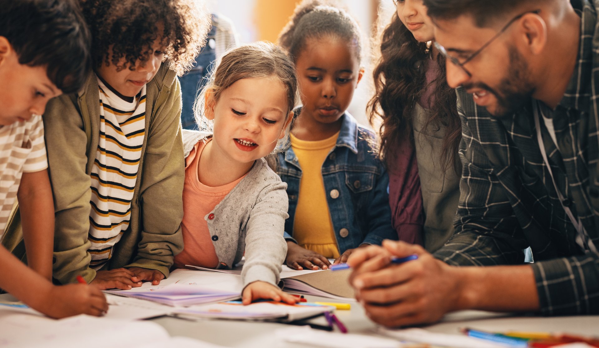 Kinder und Erwachsene arbeiten gemeinsam an einem Tisch mit Papier und Stiften.