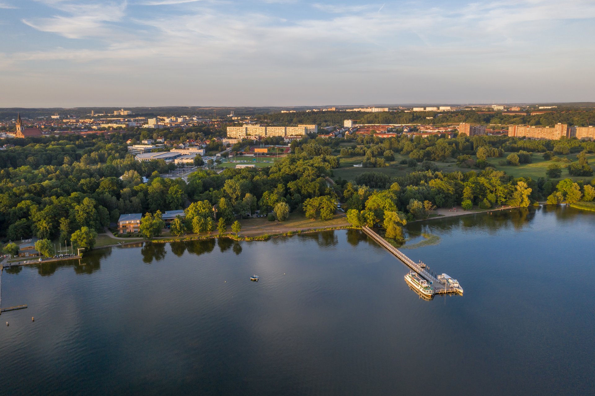 Luftaufnahme einer Stadtlandschaft mit viel Grün an einem See und einer Steganlage